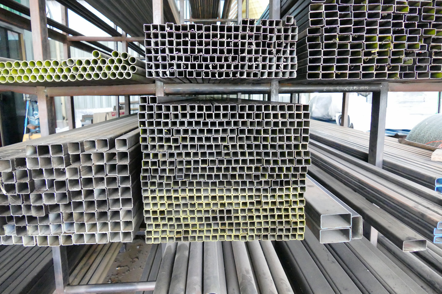Stacks of metal rectangular tubes on a metal shelf in an industrial setting