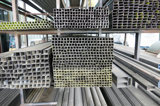 Stacks of metal rectangular tubes on a metal shelf in an industrial setting